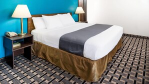 Een hotelkamer met een groot bed, twee bedlampen, een nachtkastje met telefoon en een kamerbreed tapijt met dessin.