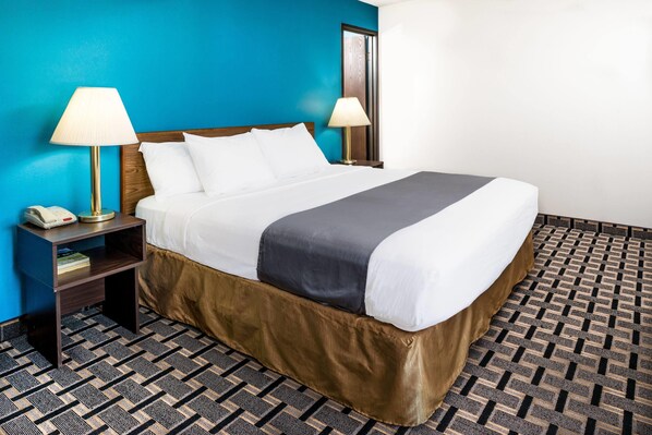 A hotel room with a large bed, two bedside lamps, a nightstand with a phone, and a patterned carpet.