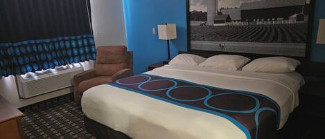 A hotel room with a large bed, a chair, a desk, and a window with curtains.