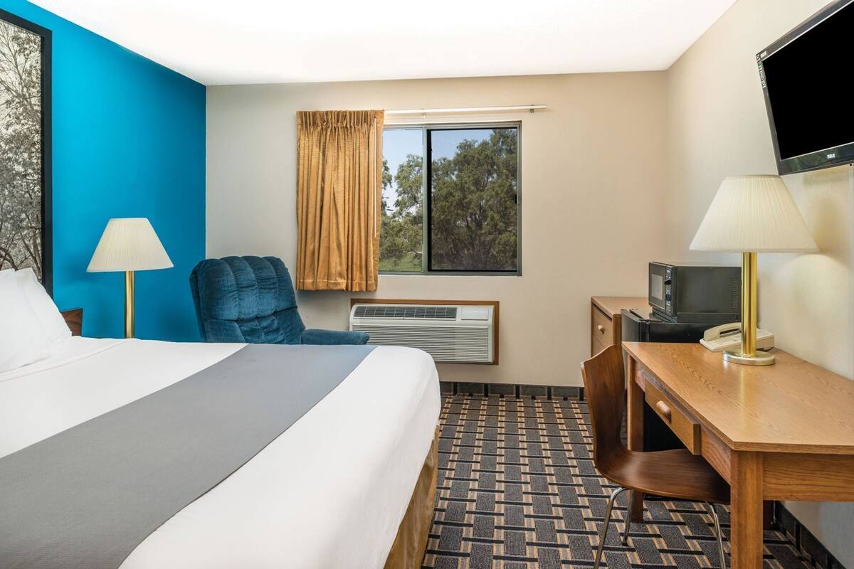 Een hotelkamer met een bed, een bureau, een stoel, een televisie, een lamp en een raam met gordijnen.