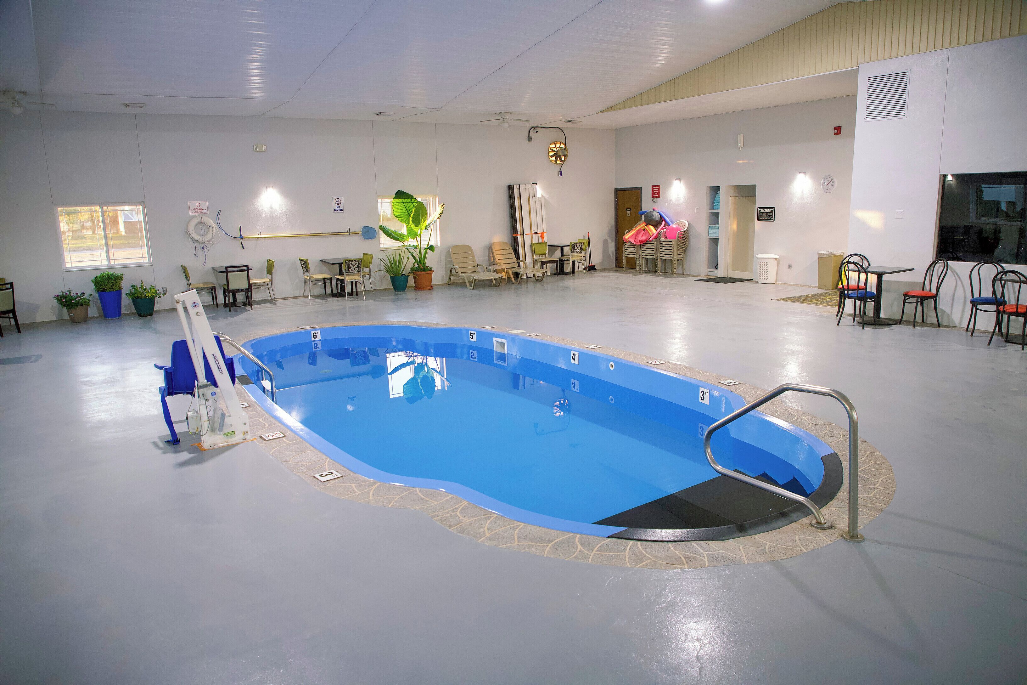 An indoor swimming pool with a blue water feature, surrounded by lounge chairs and tables, and a ceiling fan.