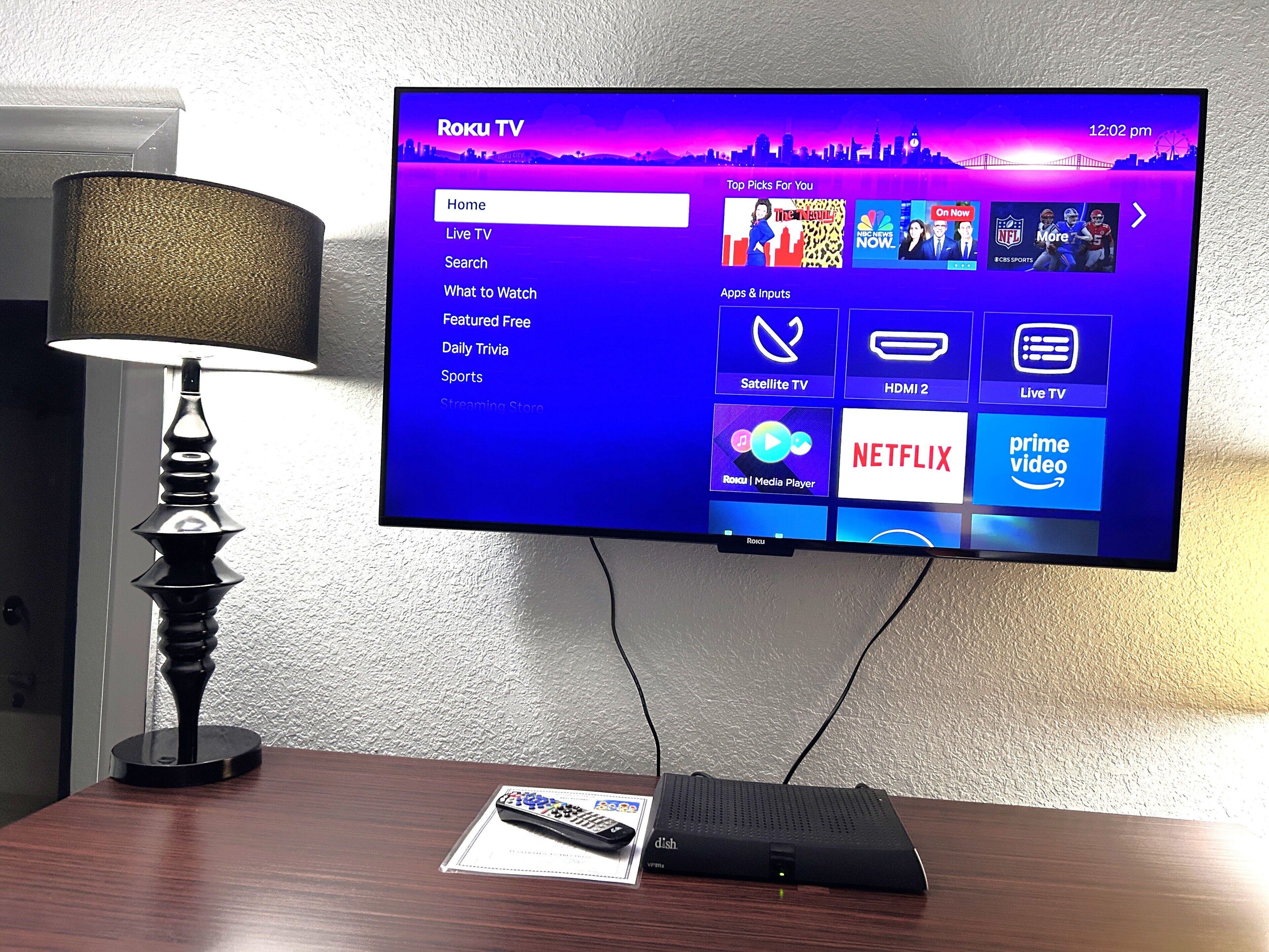 A Roku TV mounted on a wall displaying the Roku TV interface with various menu options.