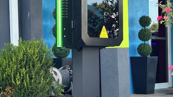 A security kiosk with a warning sign, a potted plant, and a building with a blue and yellow facade.
