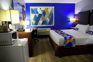 Una habitación de hotel con una cama, un escritorio con una computadora, un microondas y una obra de arte geométrica de gran tamaño.