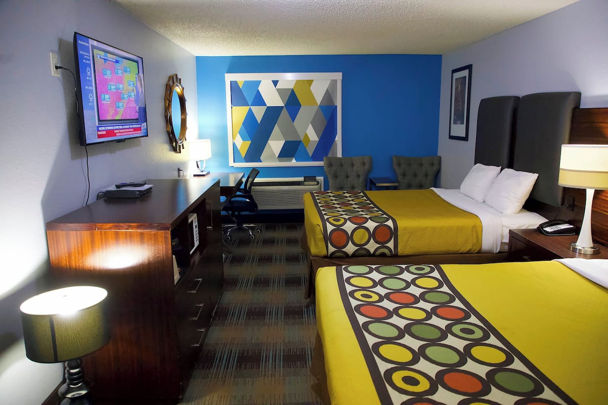 A hotel room with a desk, two beds, a TV, and a large abstract painting on the wall.