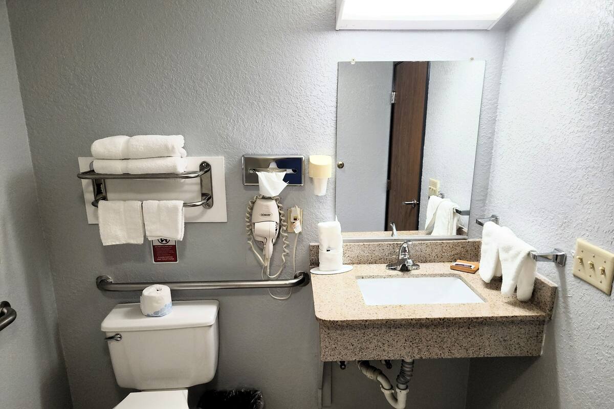 A bathroom with a toilet, sink, towel rack, hand dryer, and a trash bin.