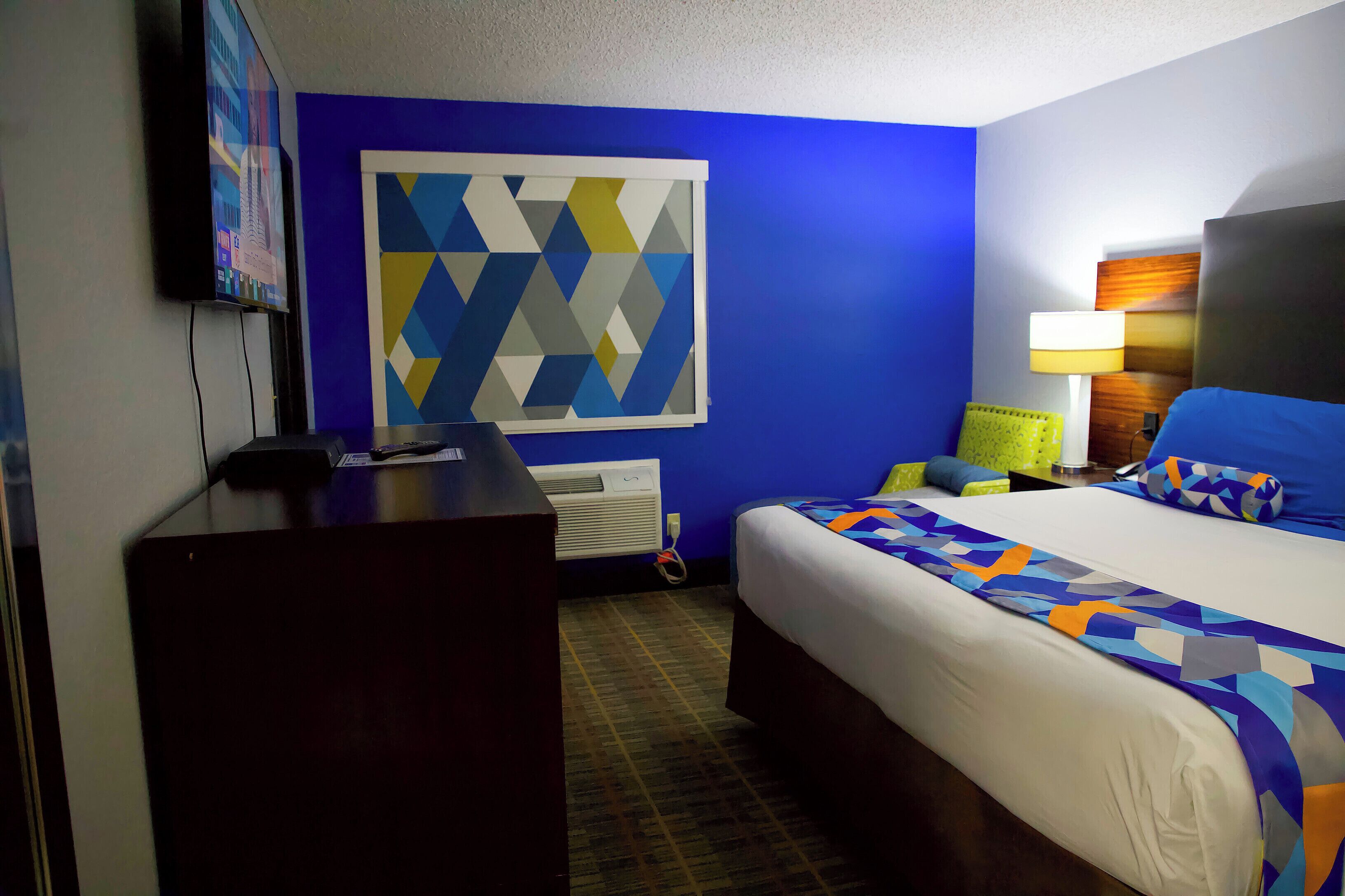 A hotel room with a bed, a desk, a TV, and a wall art piece.