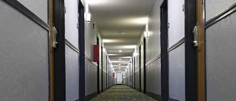 En lång, smal hotellkorridor med ett mönstrat golv, dörrar på båda sidor och takbelysning.