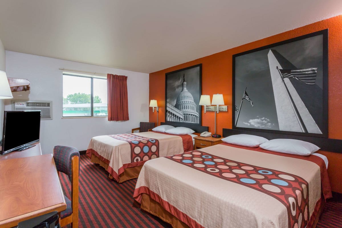 A hotel room with two beds, a TV, a desk, and a window with curtains.