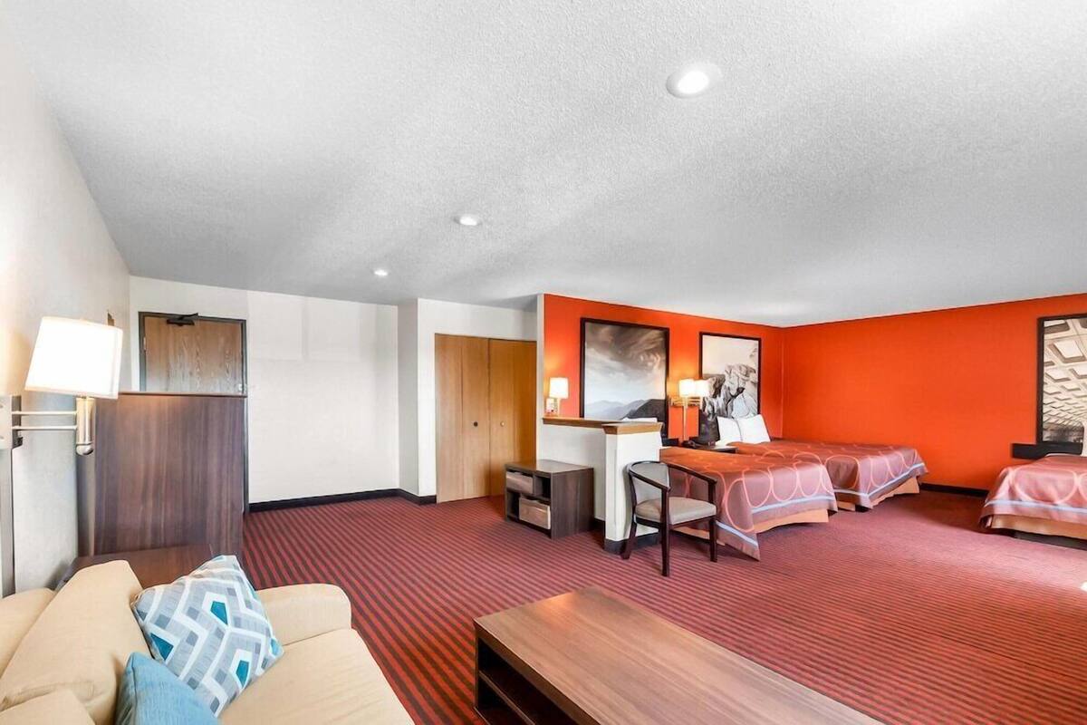 A hotel room with a sofa, a desk, two beds, and a red carpet.