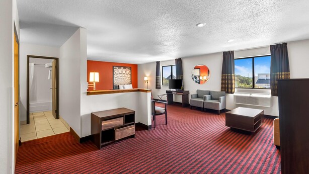 Habitación de hotel con alfombra roja, sofá, televisión, escritorio y ventana con cortinas.