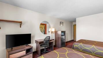 Quarto de hotel com uma cama, uma escrivaninha com cadeira, televisão, frigorífico, micro-ondas e um pequeno espelho.