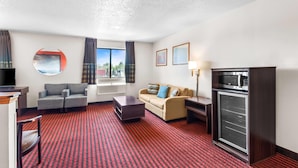 Habitación de hotel con alfombra a rayas rojas y negras, un sofá, una mesa de centro, un televisor, un microondas y una ventana con cortinas.