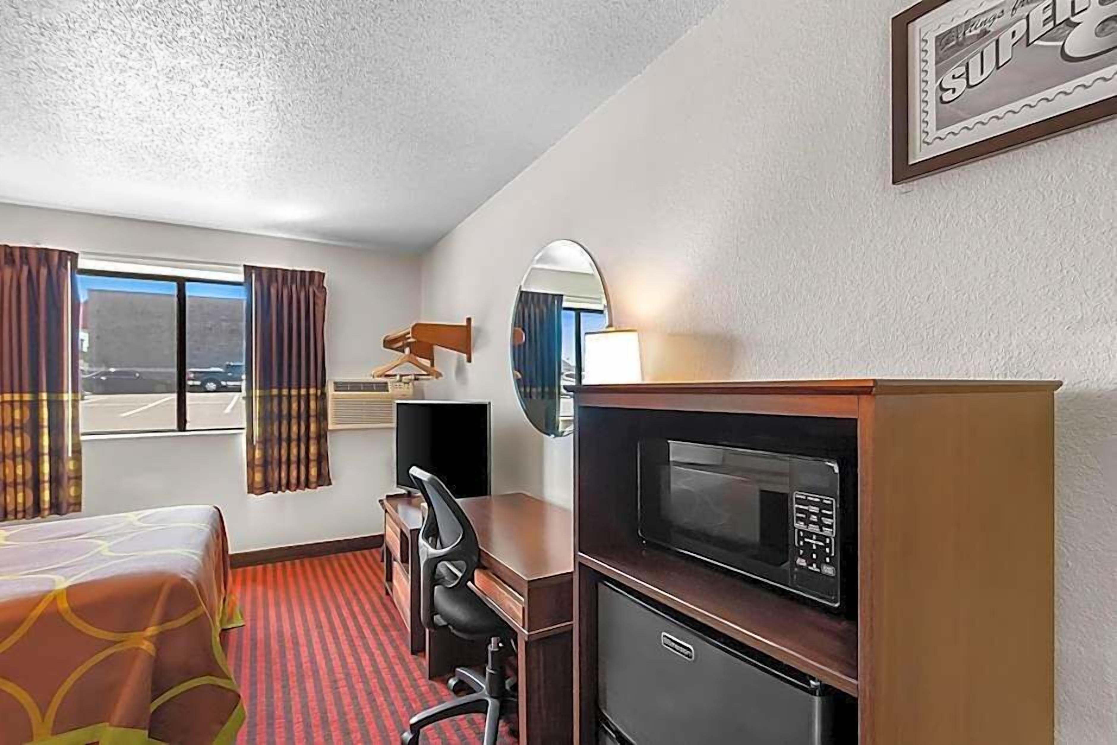 Una habitación de hotel con cama, escritorio, silla, microondas y un espejo grande.