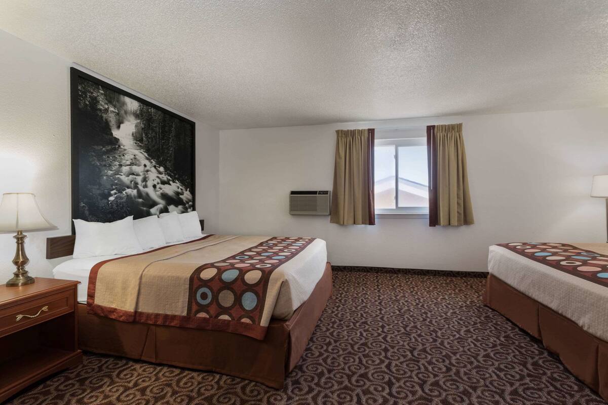 A hotel room with two beds, a large framed picture on the wall, an air conditioning unit, and a window with curtains.