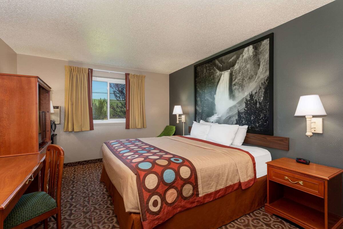 A hotel room with a bed, a desk, a chair, a nightstand, and a large painting on the wall.