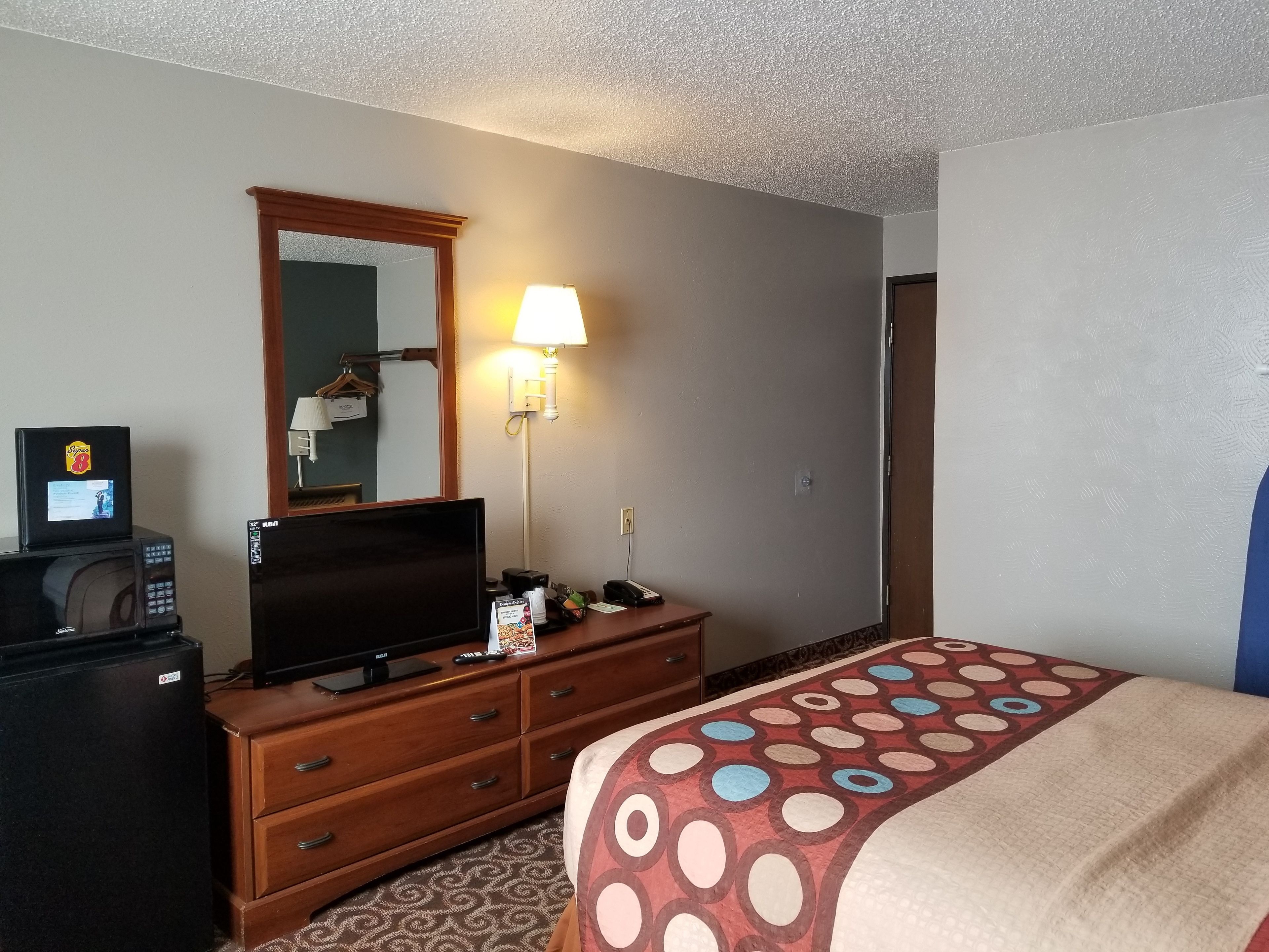 Una habitación de hotel con una cama, un tocador, un televisor, un microondas y una lámpara.