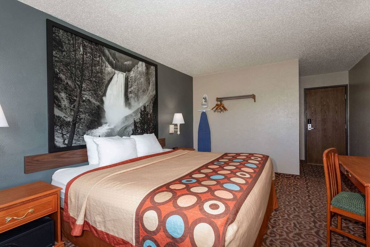 A hotel room with a bed, a desk, a chair, a wall-mounted lamp, and a door.