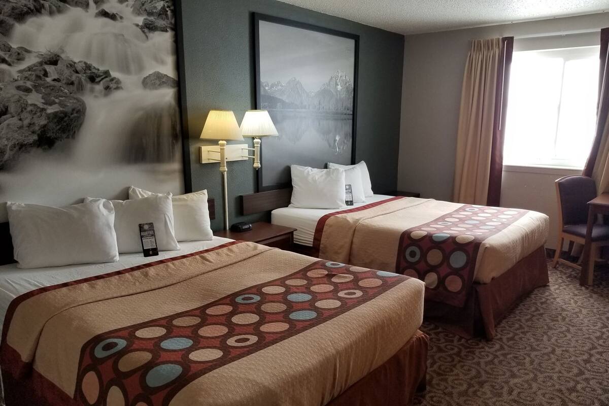 A hotel room with two beds, a large wall-mounted artwork, a desk, and a chair.