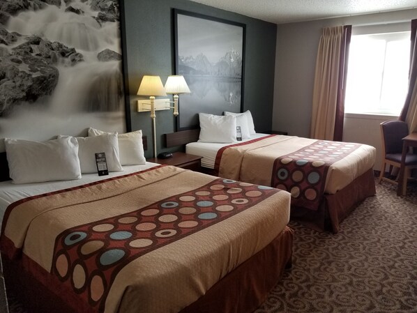 A hotel room with two beds, a large framed picture on the wall, a desk with a chair, and a window with curtains.