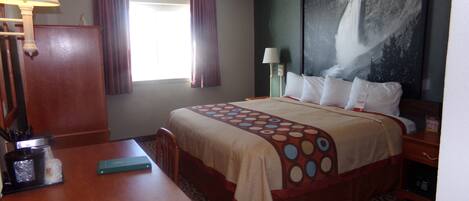 Habitación de hotel con cama, escritorio, teléfono, lámpara y un cuadro en la pared.