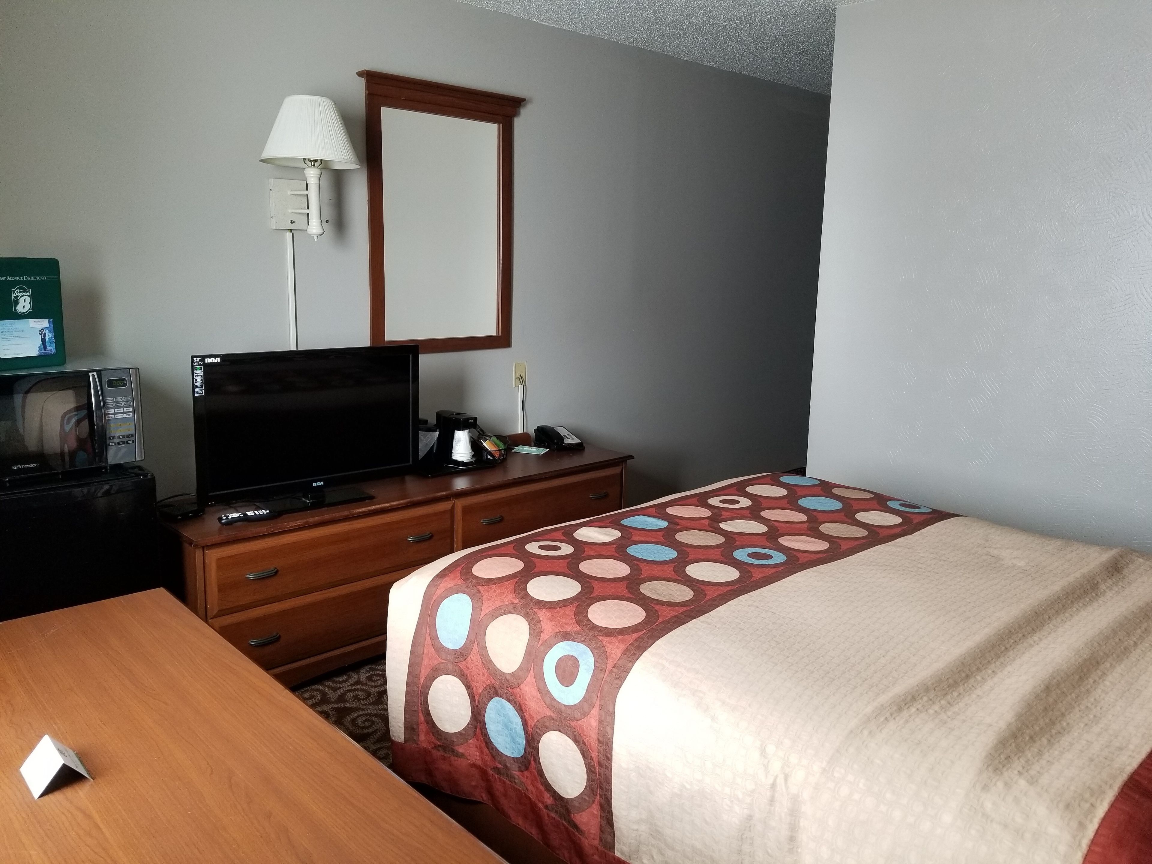 A hotel room with a bed, a TV, a desk, a lamp, and a microwave.