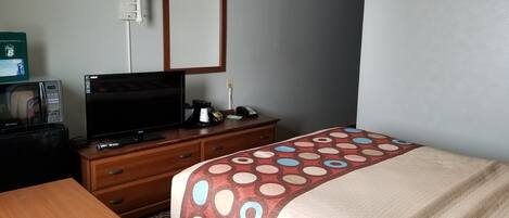 A hotel room with a bed, a TV, a desk, a lamp, and a microwave.