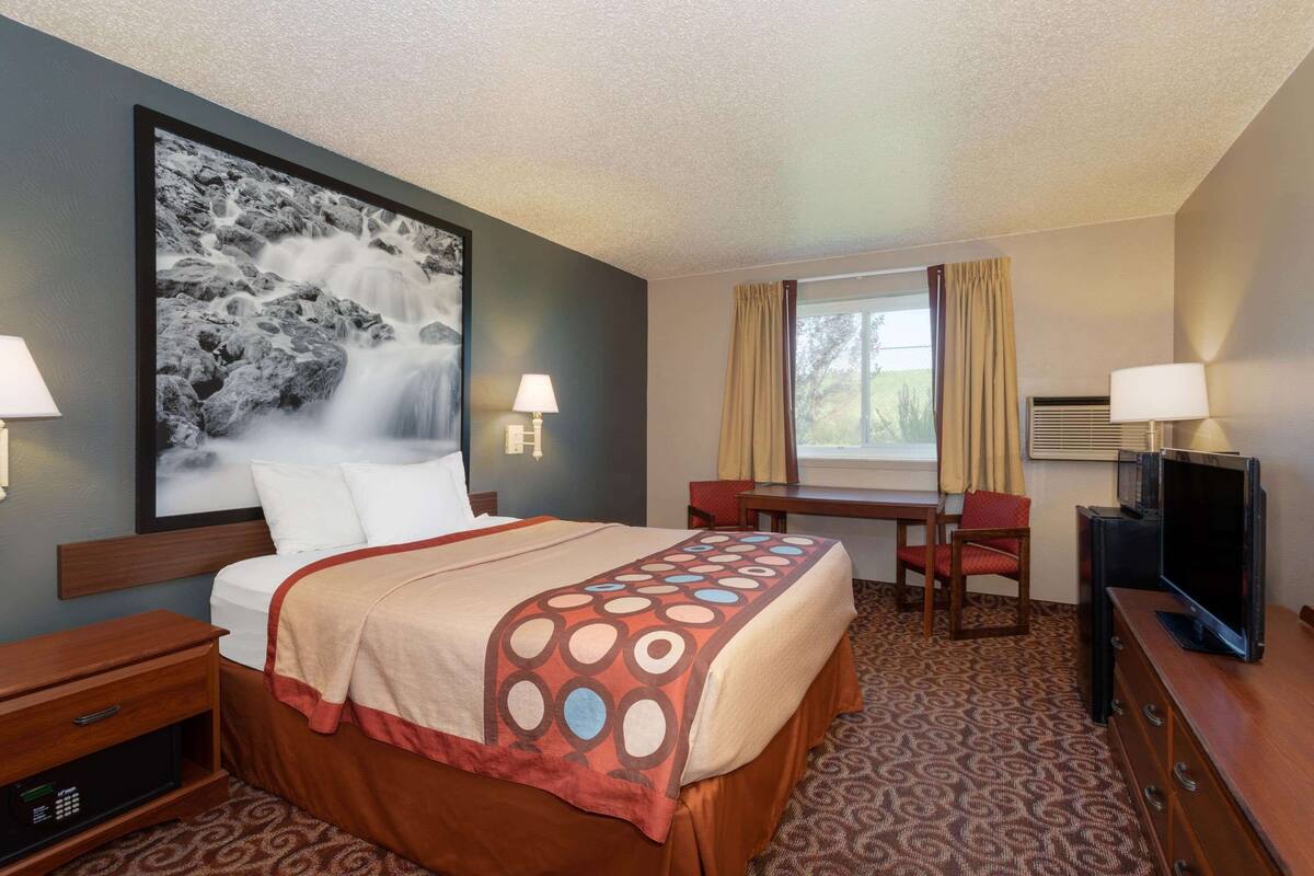 A hotel room with a bed, a desk, a television, and a large painting on the wall.