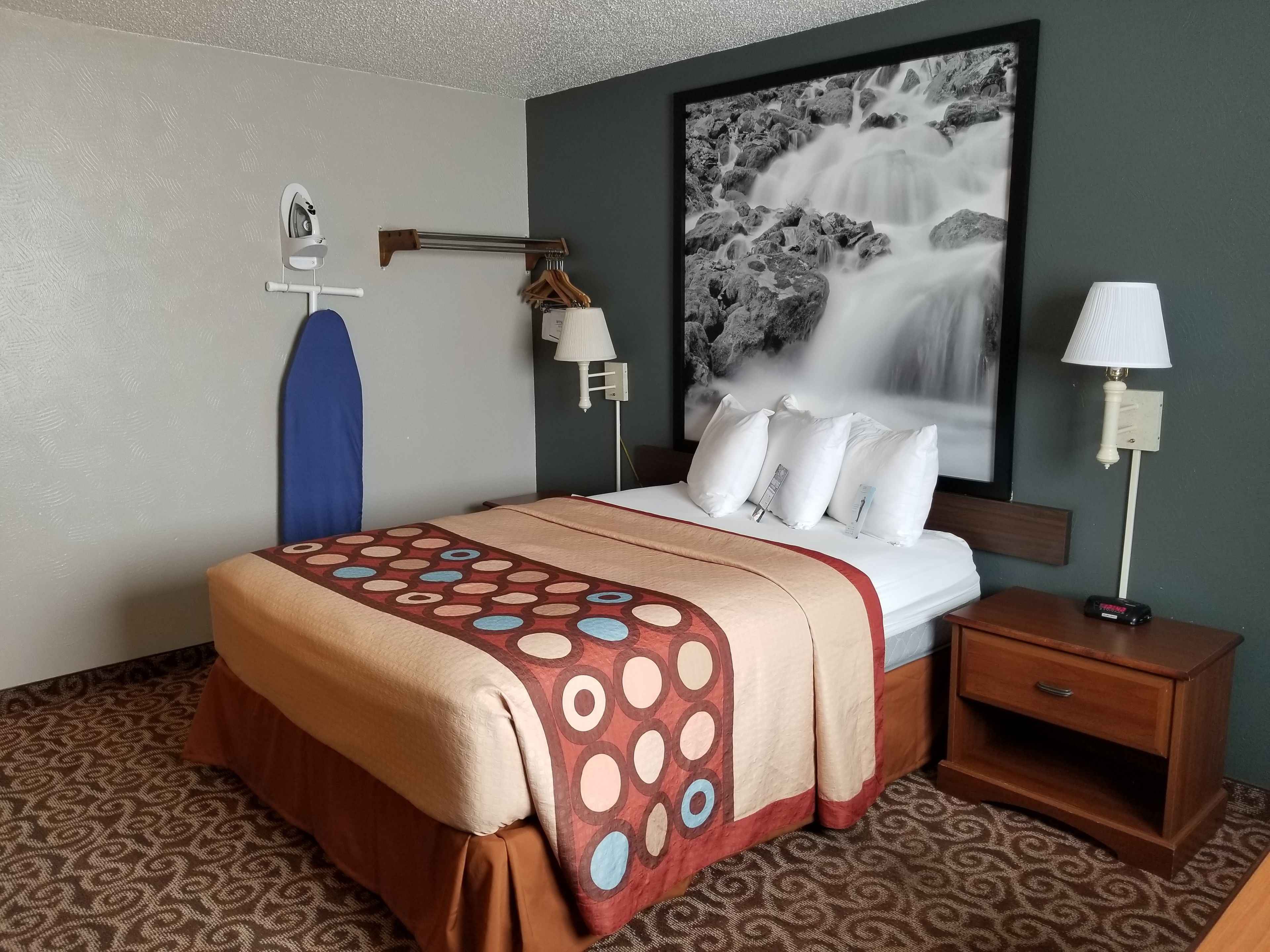 A hotel room with a bed, a nightstand, a lamp, a wall-mounted TV, and a large framed picture of a waterfall.