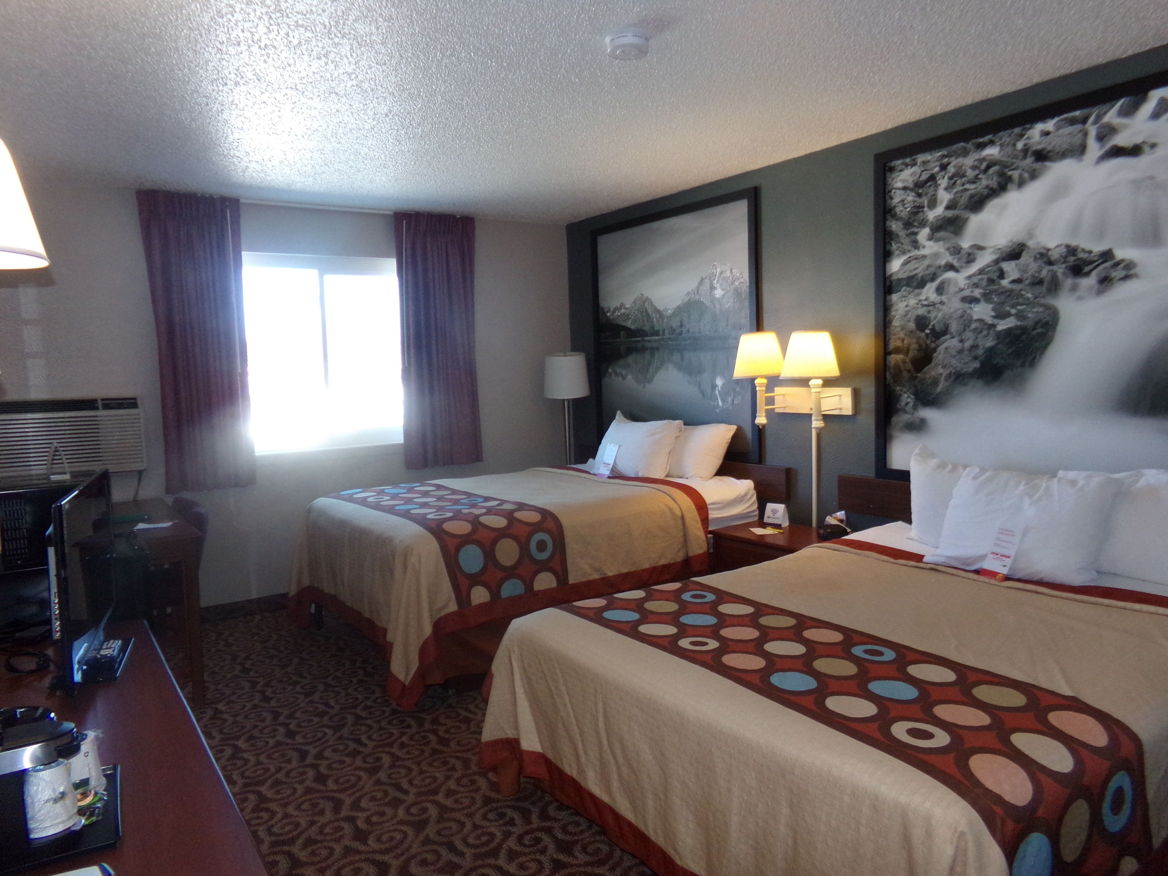 A hotel room with two beds, a desk, a lamp, and a painting of a waterfall.