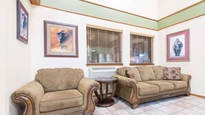 A living room with two brown sofas, a small round table, and three windows with blinds.