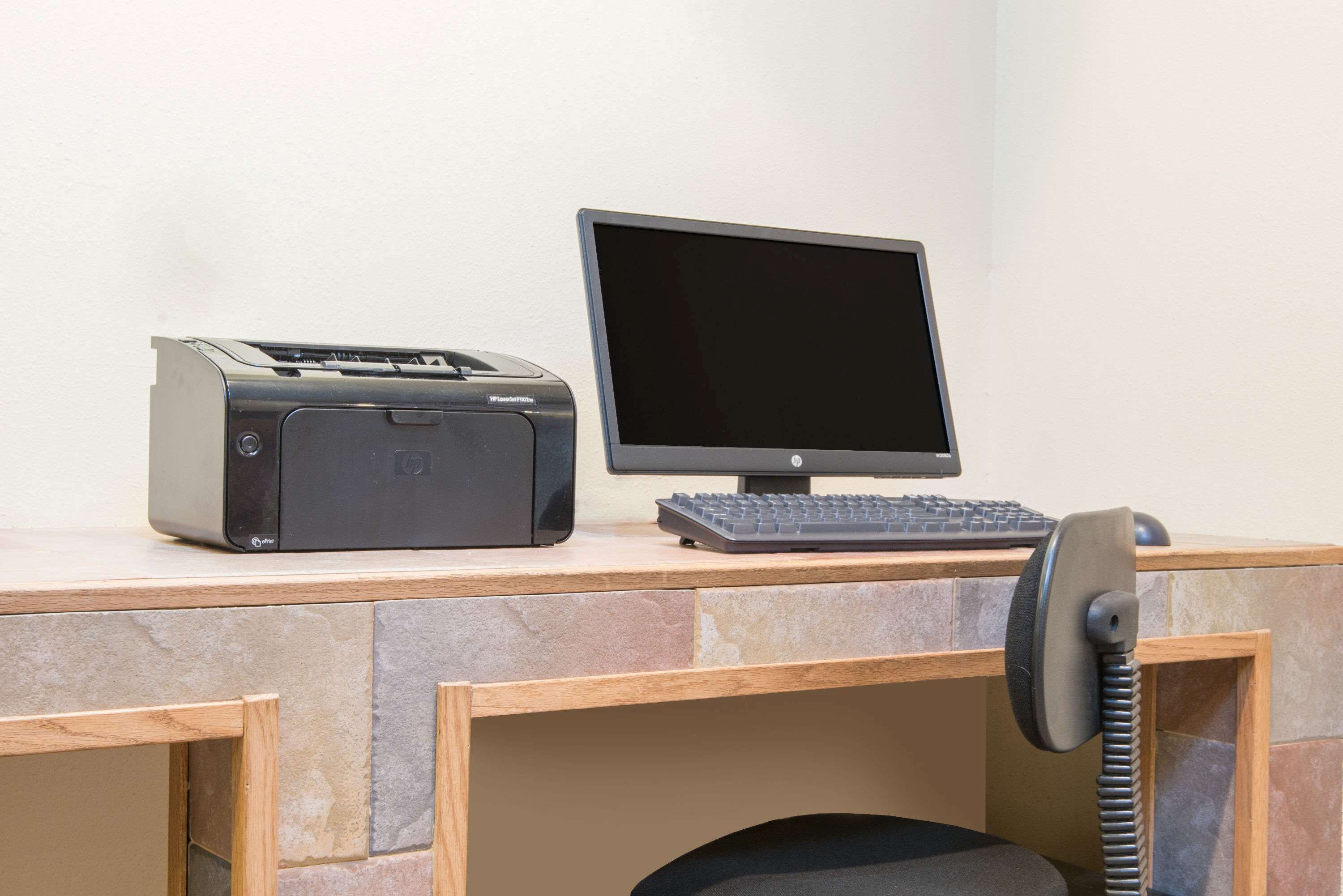 A desk with a printer, monitor, keyboard, and telephone.