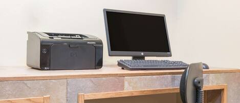 A desk with a printer, monitor, keyboard, and telephone.