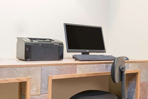 A desk with a printer, monitor, keyboard, and telephone.