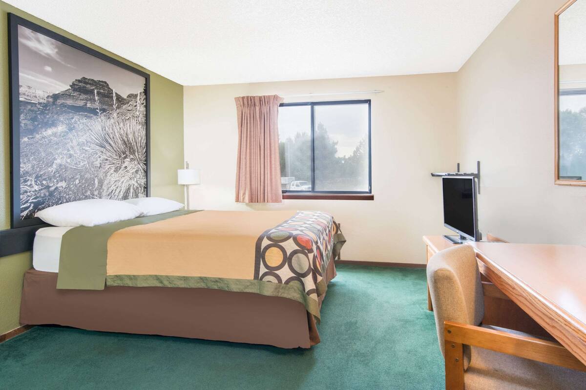 Ein Hotelzimmer mit Bett, Schreibtisch, Fernseher und einem Fenster mit Vorhängen.