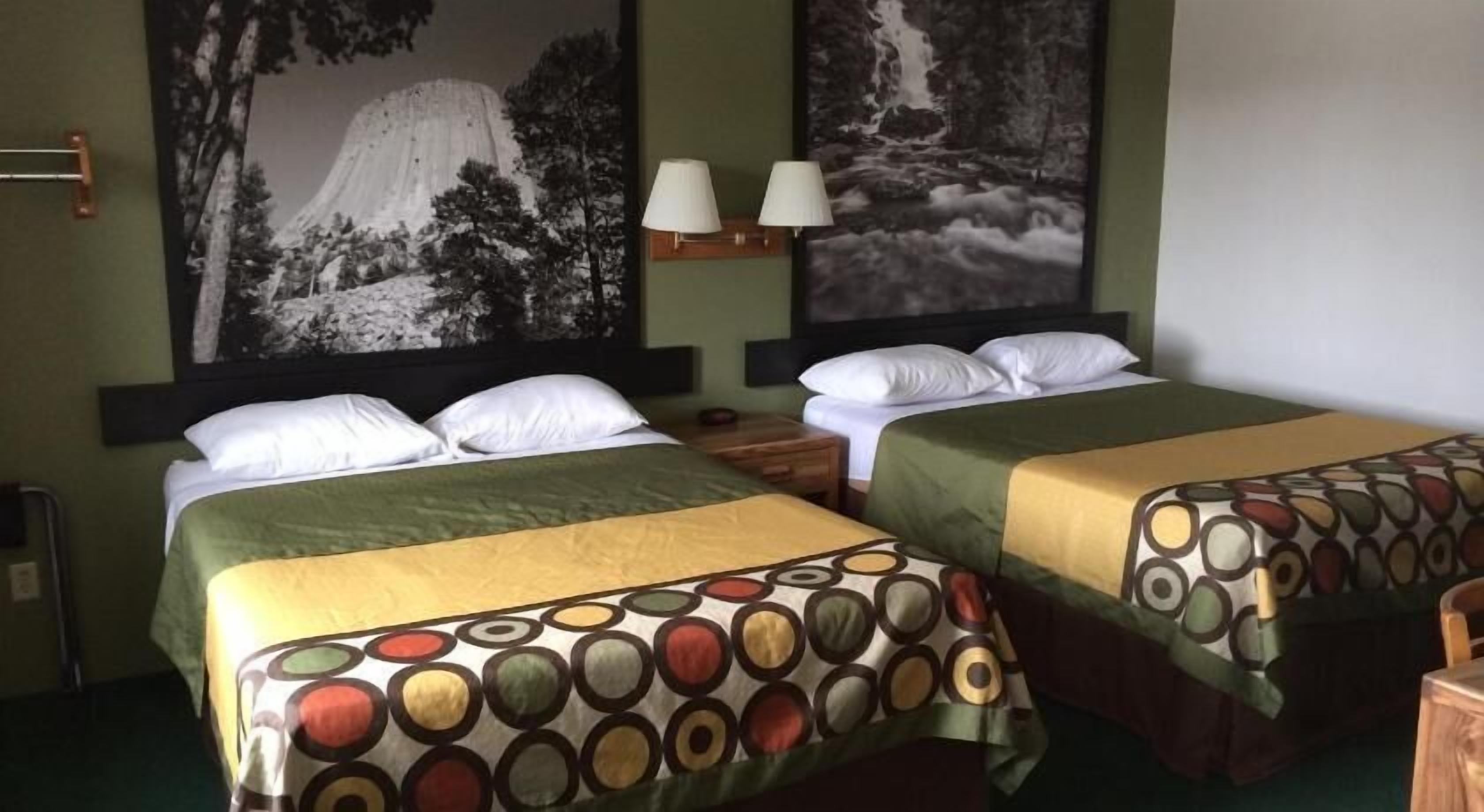 A hotel room with two beds, each with a patterned bedspread, a nightstand with a lamp, and a large wall painting of a mountain and waterfall.