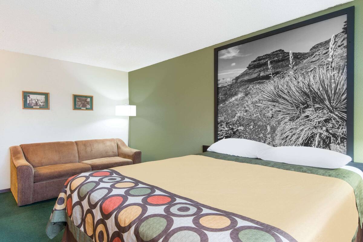 Ein Hotelzimmer mit einem Bett, einer Couch, einem großen gerahmten Bild an der Wand und zwei kleinen gerahmten Bildern an der Wand.