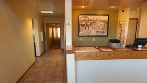 A hotel reception area with a reception desk, a framed welcome sign, a non-smoking sign, and a hallway leading to other rooms.