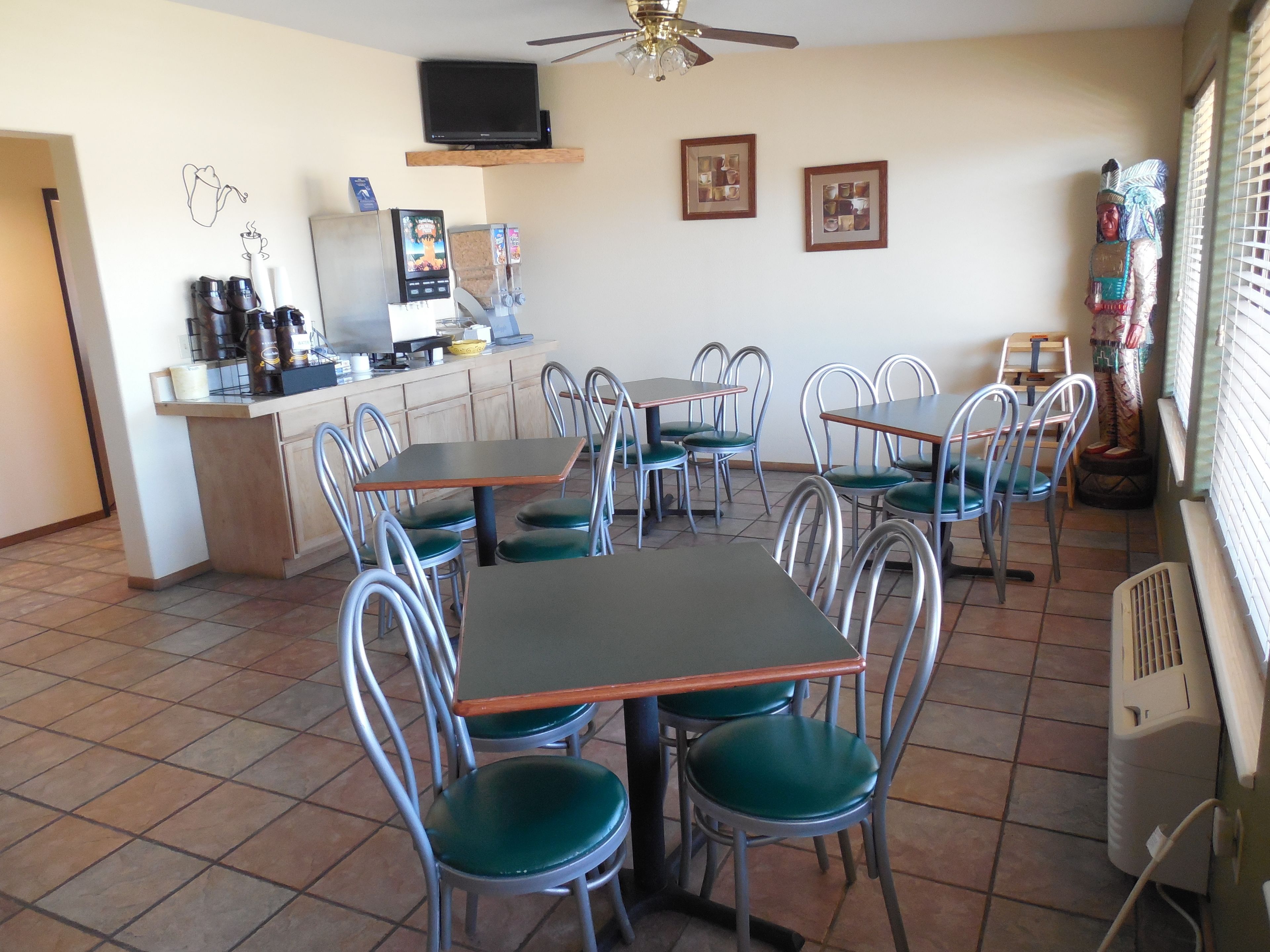 Un espace repas avec des chaises et des tables en métal, une machine à café, un téléviseur et des tableaux encadrés accrochés au mur.