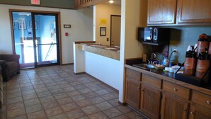 A hotel lobby with a reception desk, a coffee station, and a view of the outside through a glass door.