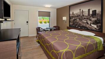 A hotel room with a bed, a desk with a television, a chair, and a window with a cityscape view.