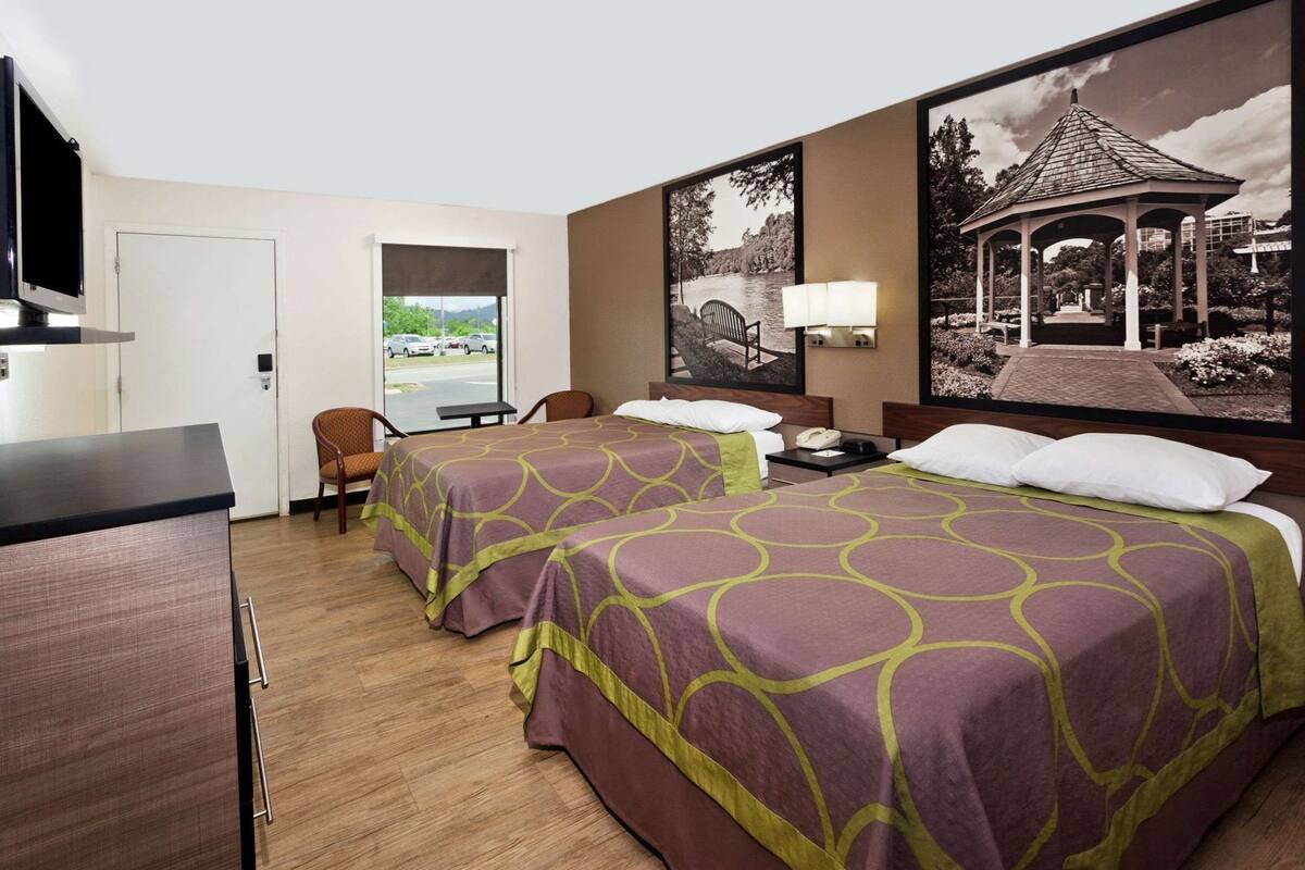 Une chambre d’hôtel avec deux lits, un bureau, une chaise, une télévision et une grande fenêtre donnant sur un parc et un kiosque.