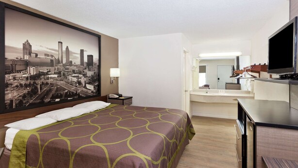 A hotel room with a large bed, a desk, a television, and a cityscape painting on the wall.