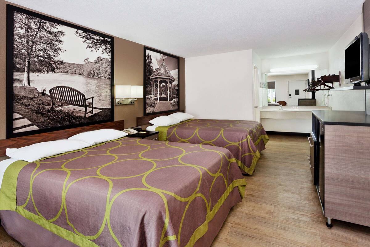Une chambre d’hôtel avec deux lits, un bureau, une télévision et des œuvres d’art accrochées aux murs.