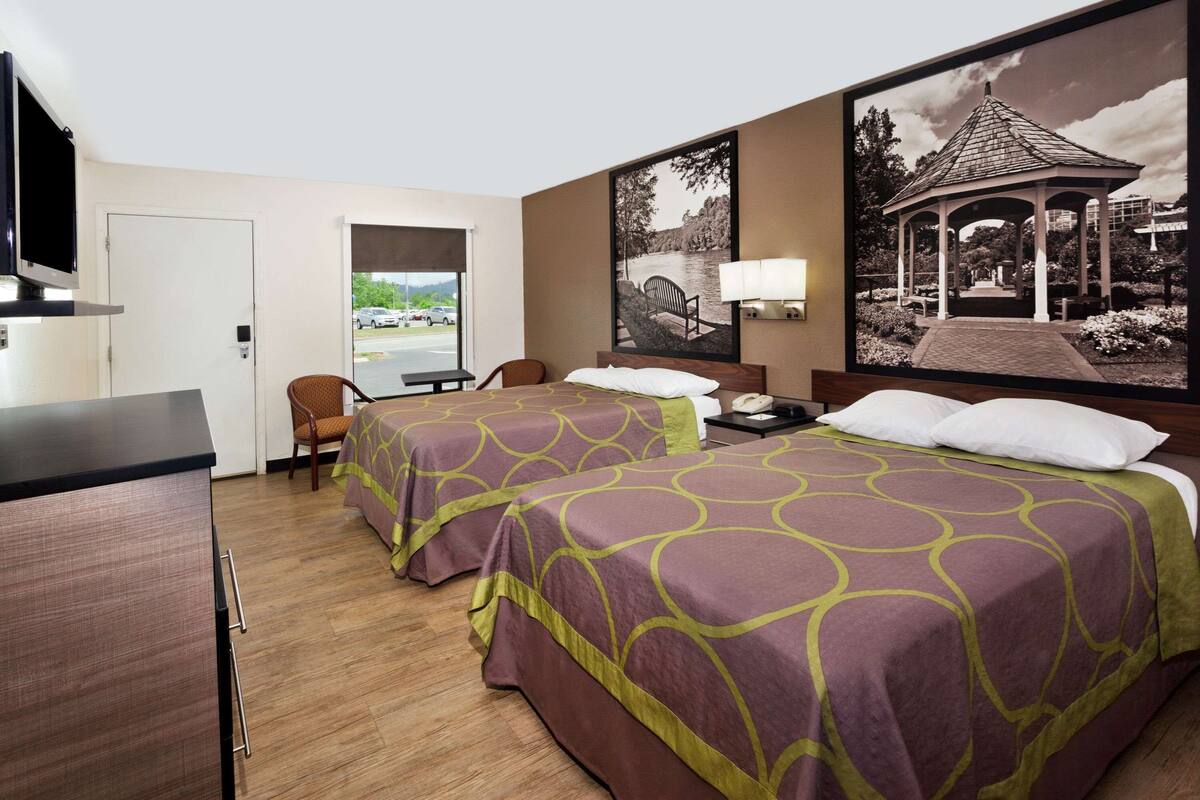 Une chambre d’hôtel avec deux lits, un bureau, une chaise, une télévision et une grande fenêtre donnant sur un parc et un kiosque.
