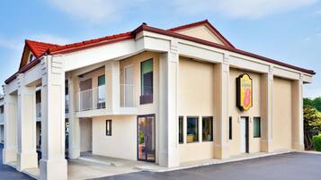 A hotel with a beige facade, a red roof, and a prominent 'Super 8' sign. It features a balcony on the second floor and a covered entrance.