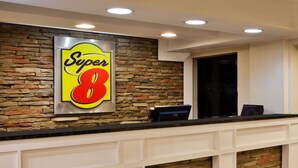 A reception desk with a 'Super 8' sign, a stone wall, and a modern ceiling with recessed lighting.