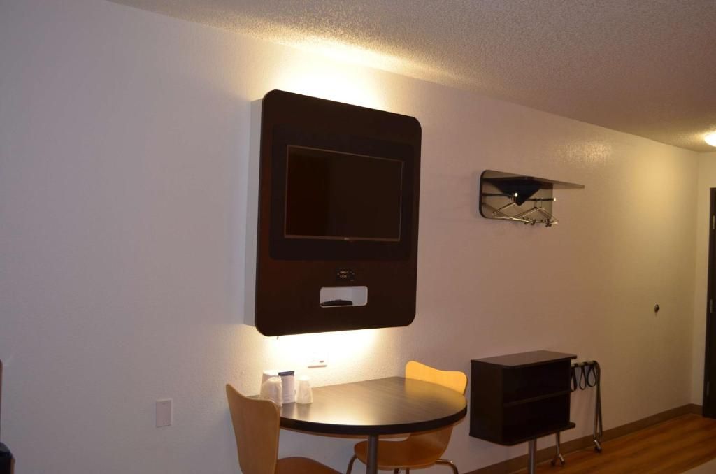 A room with a round table, two chairs, a wall-mounted TV, and a small shelf.