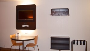 A small room with a round table, two chairs, a TV mounted on the wall, a coat rack, and a small cabinet. - Motel 6 Kingsland, GA - Kings Bay Naval Base (Kingsland)