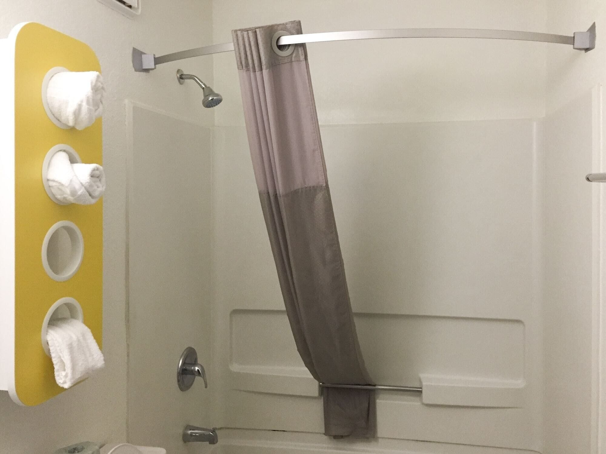 A bathroom with a shower, a towel rack with multiple towels, and a curtain rod.